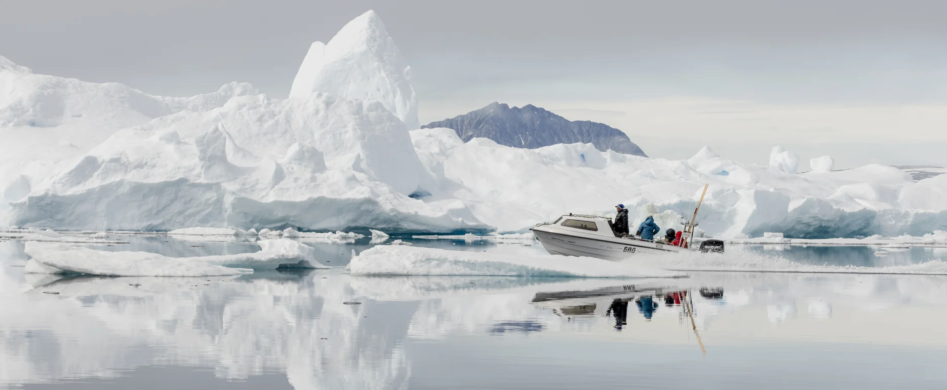 Boat navigating through calm waters surrounded by large icebergs in East Greenland. Photo by Oscar Scott Carl - Visit East Greenland
