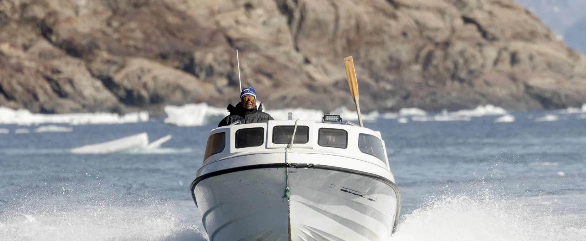 Boat navigating through the icy waters of East Greenland with mountains and icebergs in the background. Photo by Oscar Scott Carl - Visit East Greenland