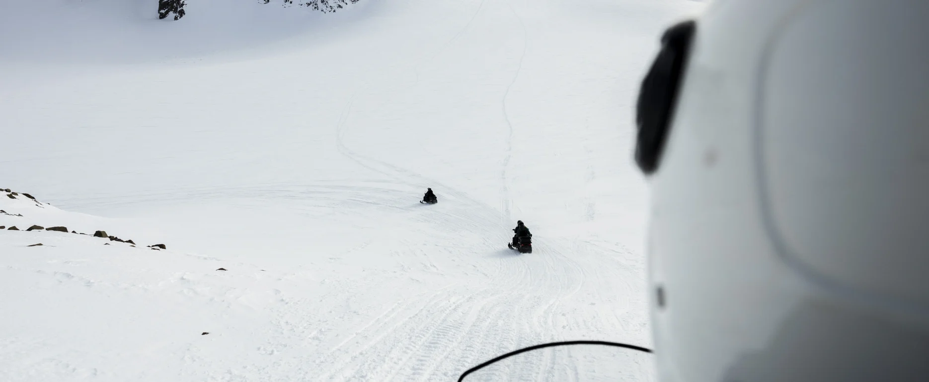 Snowmobiles Ascending Snowy Slopes Towards East Greenland’s Majestic Peaks.