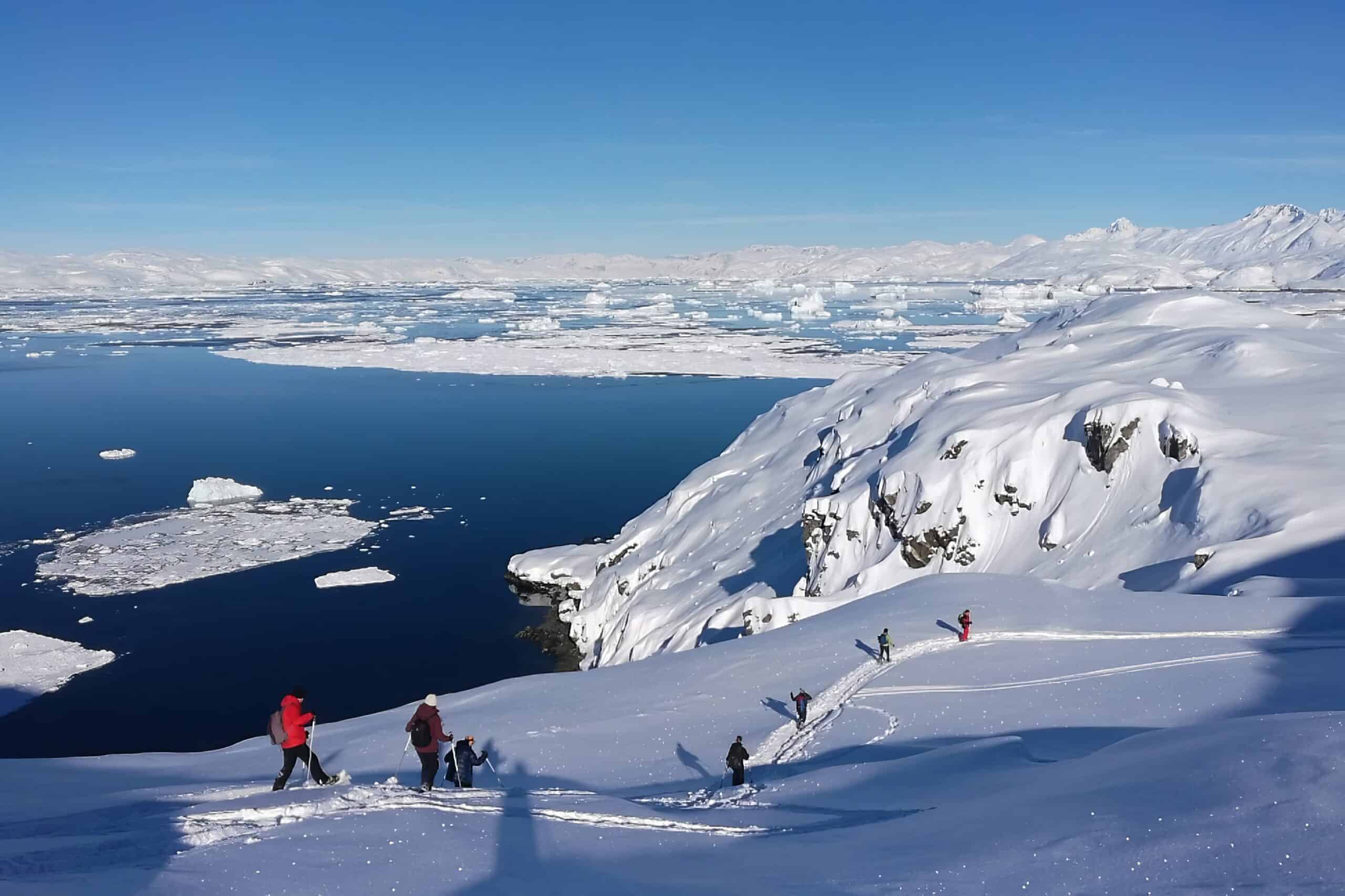 A group of tourists on a snowshoe hike on Ammassalik island overlooking Sermilik Fjord.